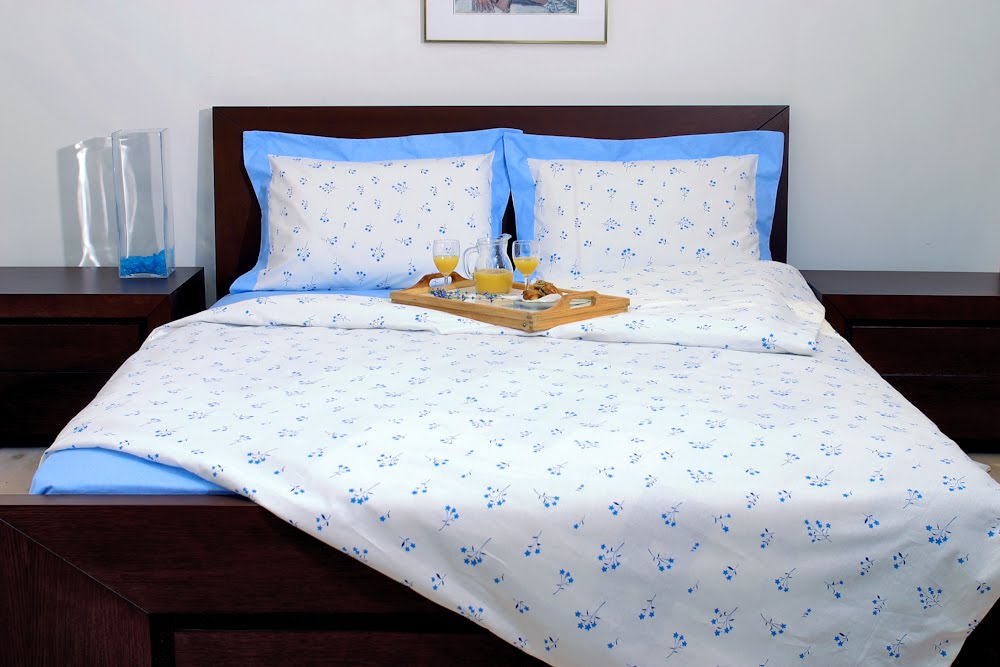 A clean, commercial studio photograph of a neatly made bed featuring white bedding with a blue floral pattern and a breakfast-in-bed tray.